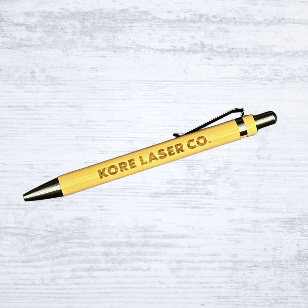 Eco-friendly bamboo pen engraved with the Kore Laser Co. logo in bold lettering on a white-washed wood background.