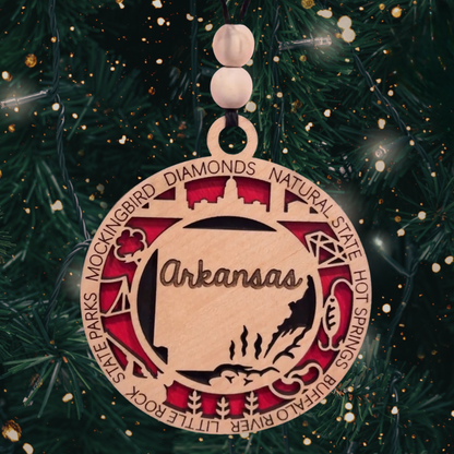 Round multi-layer laser cut ornament featuring an outline of the state of Arkansas and a number of descriptive words.
