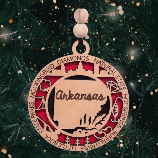 Round multi-layer laser cut ornament featuring an outline of the state of Arkansas and a number of descriptive words.