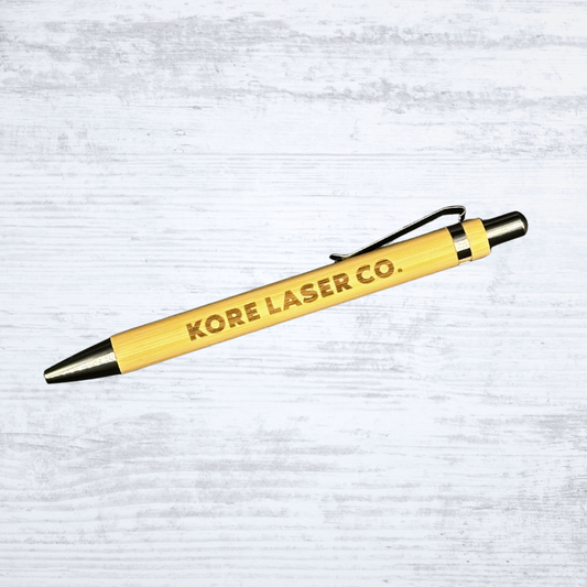 Eco-friendly bamboo pen engraved with the Kore Laser Co. logo in bold lettering on a white-washed wood background.