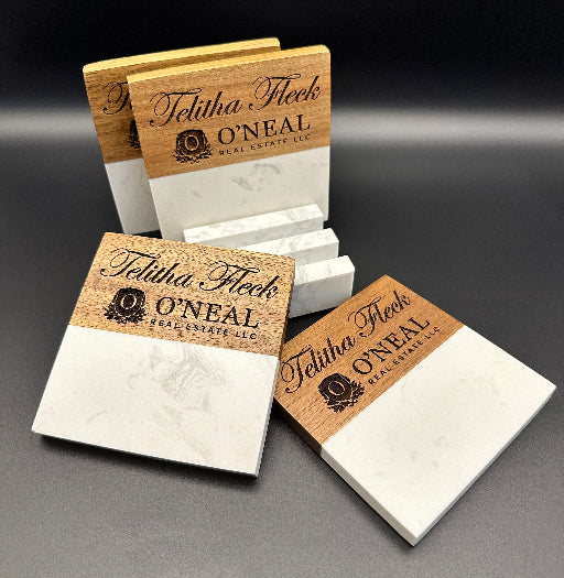 Set of square coasters with a wood and white marble design, neatly arranged upright in a matching marble stand. The coasters are engraved with a realtor’s name and agency affiliation, displayed against a dark background.